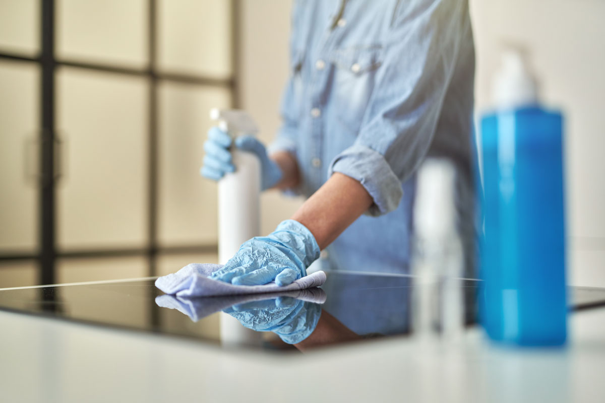 Person wearing gloves wiping a stovetop, demonstrating standard cleaning.